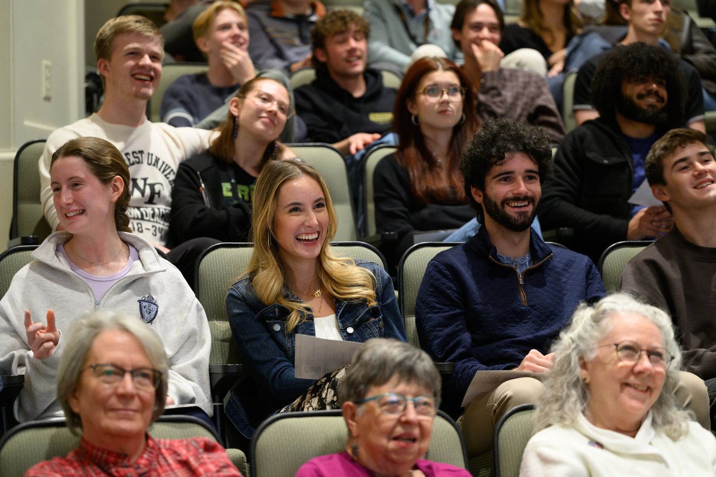 College students and older adults laughing together in an auditorium audience.